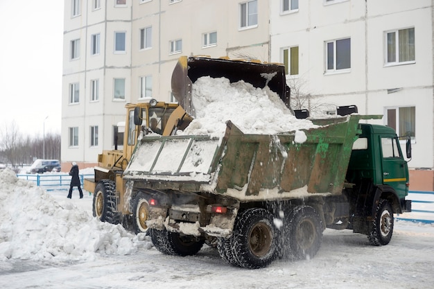 Трактор загружает в кузов автомобиля снег, собранный во дворе