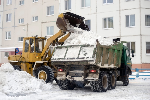 Трактор загружает в кузов автомобиля снег, собранный во дворе