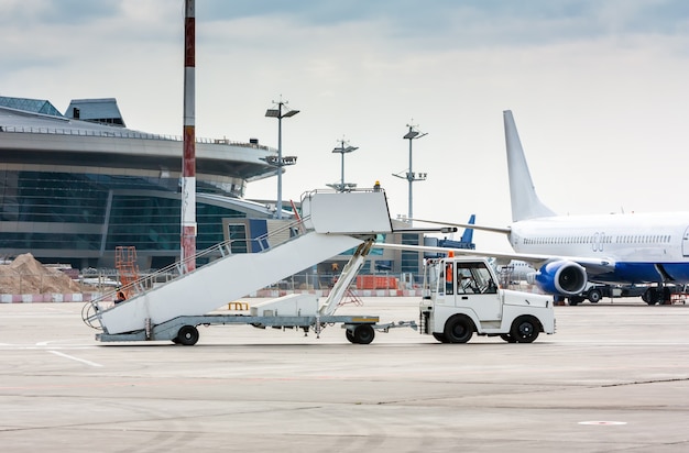 Il trattore tira le scale di imbarco dei passeggeri presso il piazzale dell'aeroporto accanto al terminal