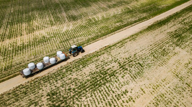 Photo tractor rides on the field and carries bales of hay aerial view