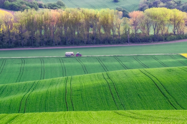 Tractor rides on road along green fields, agricultural landscape