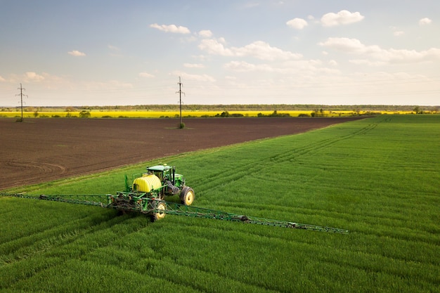 Photo tractor spraying chemical pesticides with sprayer on the large green agricultural field at spring.