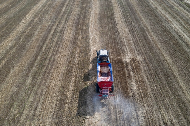 Tractor spreading artificial fertilizers in field. Top view.