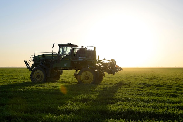 Photo tractor on the sunset background tractor with high wheels is making fertilizer on young wheat the use of finely dispersed spray chemicals