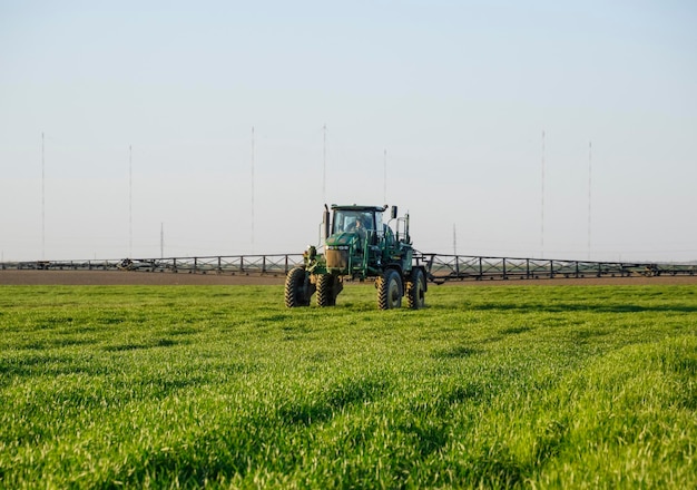 Photo tractor on the sunset background tractor with high wheels is making fertilizer on young wheat the use of finely dispersed spray chemicals