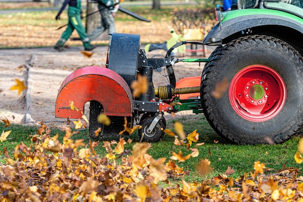 送風機付きのトラクターが都市公園の芝生を掃除し、紅葉のクローズアップを吹き飛ばします