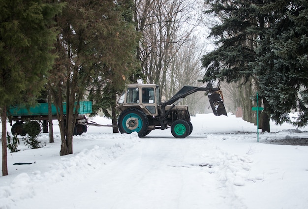 Трактор с прицепом зимой в ботаническом саду расчищает дорогу от снега и веток.