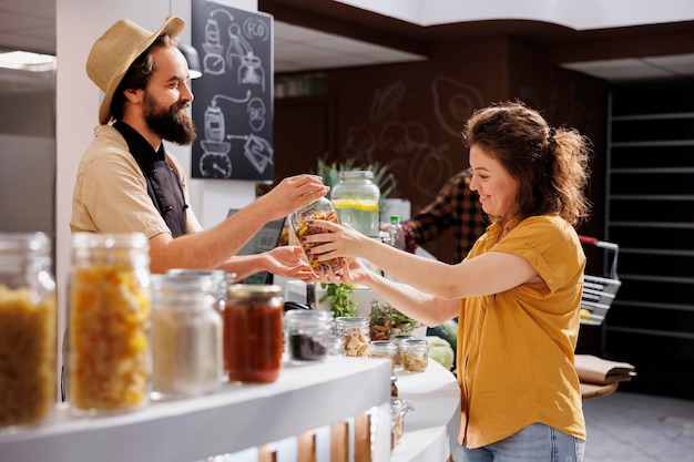 Trader at checkout counter in zero waste shop selling homemade pasta to customer with sustainable lifestyle. Client buys organic nonpolluting food in ecological local neighborhood store