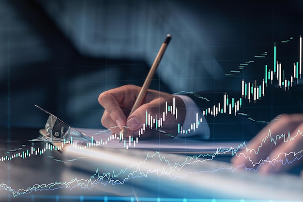 A trader in formal wear writing down some ideas to research
stock market to proceed right investment solutions wealth
management concept hologram forex chart over close up shot