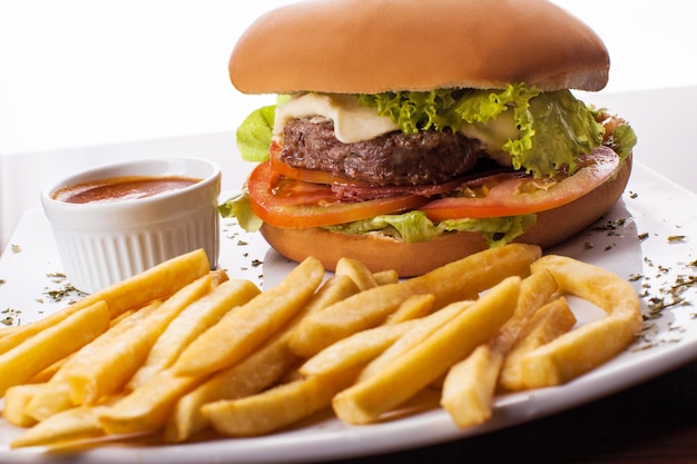 Tradicional hamburger, sauce and french fries on white plate