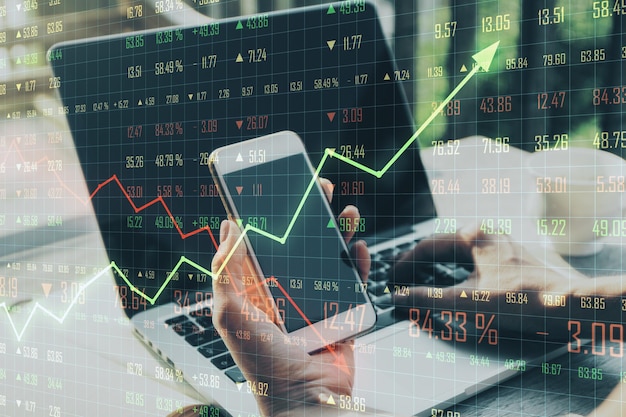 Trading concept with man holding cell phone and laptop and business chart