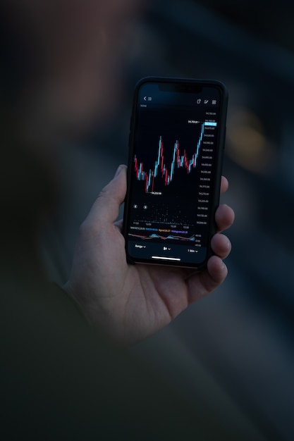 Photo trading wherever you are. male hand using mobile app on smartphone for reading financial news in real time and checking stock market data in real time. selective focus on screen with forex graph chart