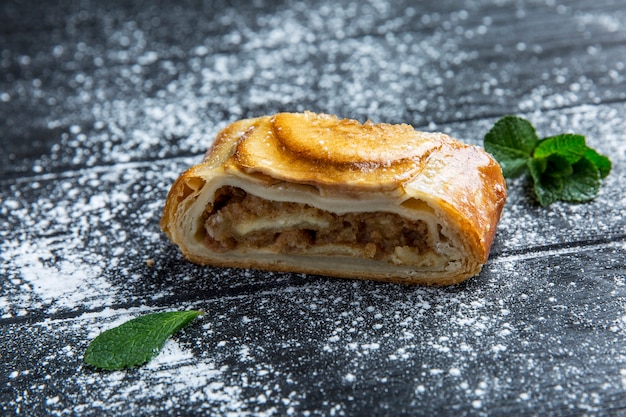 Traditional apple strudel with icing sugar on a dark wood table. Close-up.