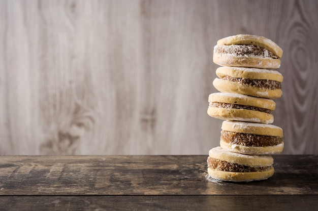 Traditional Argentinian alfajores with dulce de leche and sugar on wooden table, copy space