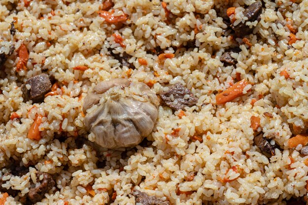 Traditional Asian culinary dish - pilaf. Ingredients: rice with slices of meat, fat and vegetables (carrot, garlic), spices- popular recipe. Close-up view of Eastern tasty food background.