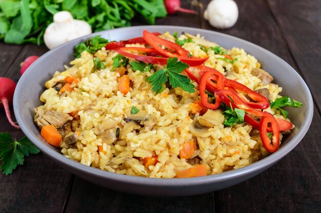 A traditional Asian dish - pilaf with meat, mushrooms and pepper capi in a bowl on a dark wooden table.