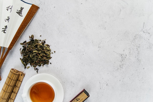 Traditional asian fan with herbal tea and rolled up placemat on concrete backdrop