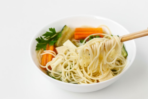 Traditional asian soup with tofu cheese, noodles, carrots and zucchini on white background