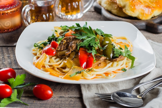 Traditional asian uzbek noodle lagman with vegetables and meat on rustic wooden table. Close-up