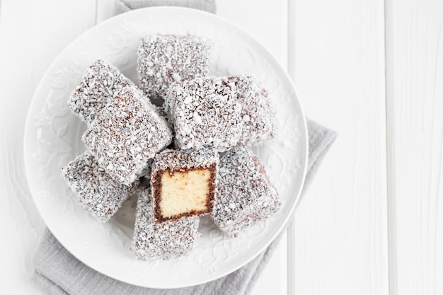 Traditional Australian Lamington cake in chocolate glaze and coconut flakes on a white plate