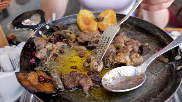 Traditional azerbaijan cuisine food in the restaurant Woman is eating meat with vegetables served in frying pan hands closeup Traditional eastern food