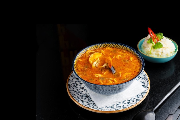 Фото Традиционный азианский суп из тома и яма на тарелке на черном фоне