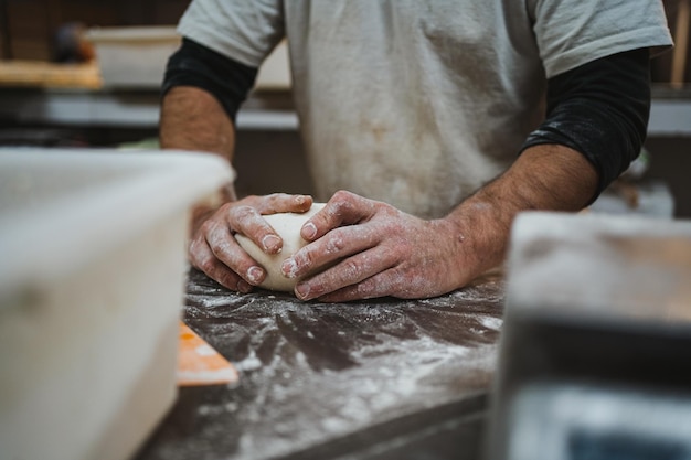 Traditional baker kneading bread dough at kitchen of a bakery