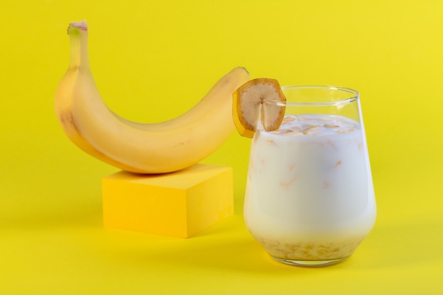 Latte di banana tradizionale in un bicchiere e banana matura sul podio giallo concetto di un'alternativa vegana al latte tradizionale