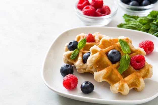 Traditional belgian waffles with blueberries and raspberries on white marble copy space