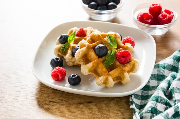 Traditional belgian waffles with blueberries and raspberries on wooden table