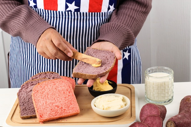 Традиционное приготовление завтрака. Руки женщины, намазывающей масло на кусок хлеба с ножом над столом с нарезанным хлебом и салфеткой. Крупный план. Хлеб или концепция еды