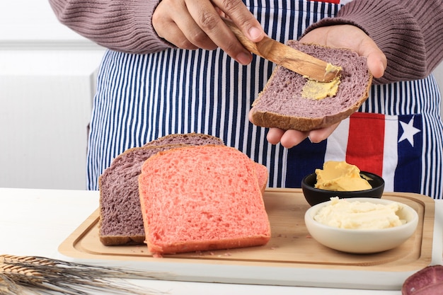 伝統的な朝食の料理。スライスされたパンとナプキンでテーブルの上にナイフでパンのスライスにバターを広げる女性の手。閉じる。パンや食事の概念