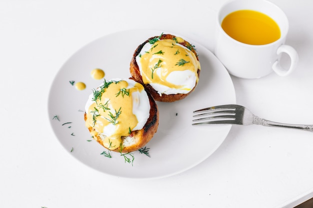 Традиционный завтрак. Яйца Бенедикт на тарелке с апельсиновым соком