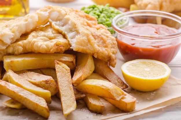 Traditional British street food fish and chips with mushy peas and ketchup sauce on parchment paper