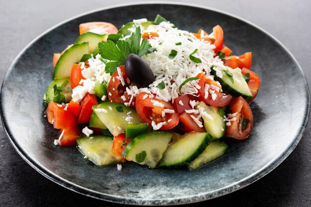 Traditional Bulgarian shopska salad with tomatocucumber and bulgarian sirene cheese on black background