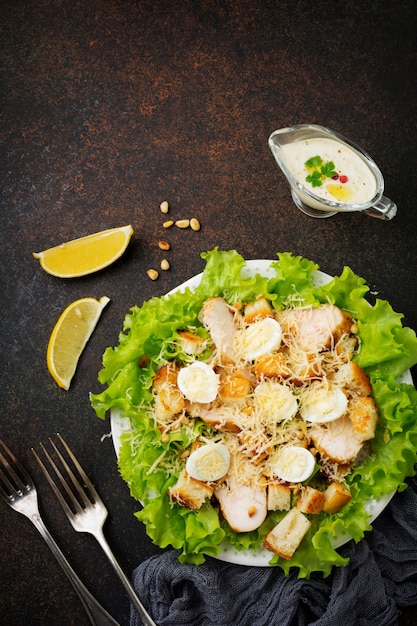 Traditional Caesar Salad with quail eggs and pine nuts in a light ceramic bowl on dark stone or concrete surface