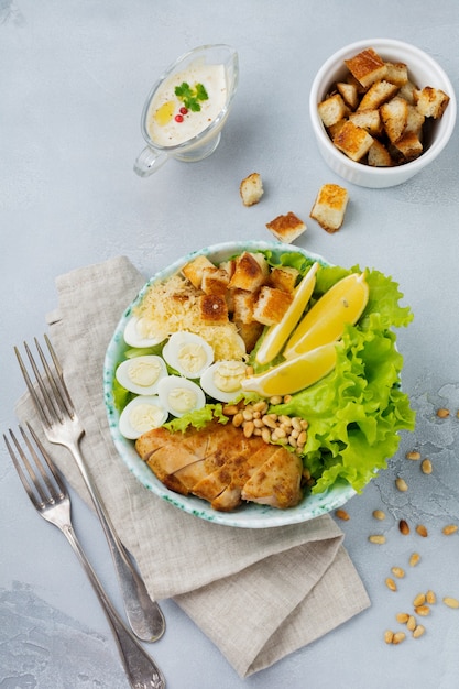 Traditional Caesar Salad with quail eggs and pine nuts in a light ceramic bowl On a gray concrete surface