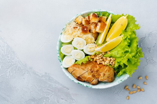 Caesar salad tradizionale con uova di quaglia e pinoli in una ciotola di ceramica leggera su una superficie di cemento grigio