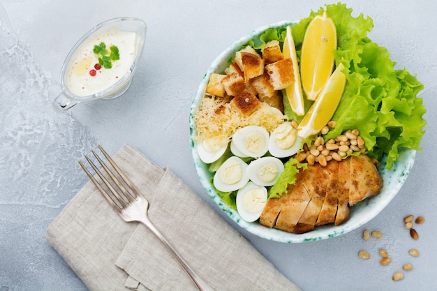 Traditional Caesar Salad with quail eggs and pine nuts in a light ceramic bowl On a gray concrete surface