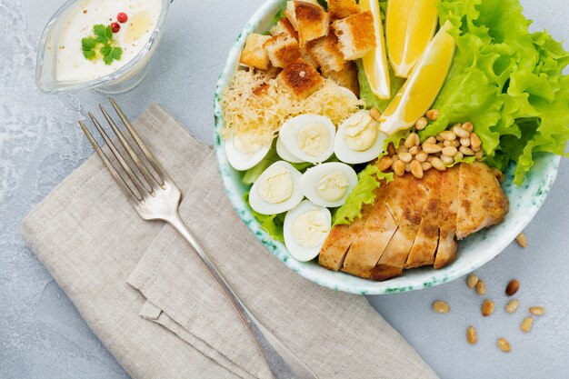 Traditional Caesar Salad with quail eggs and pine nuts in a light ceramic bowl On a gray stone or concrete surface