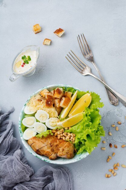 Traditional Caesar Salad with quail eggs and pine nuts in a light ceramic bowl On a gray stone or concrete surface