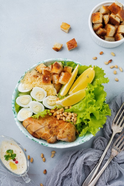 Traditional Caesar Salad with quail eggs and pine nuts in a light ceramic bowl On a gray stone or concrete surface