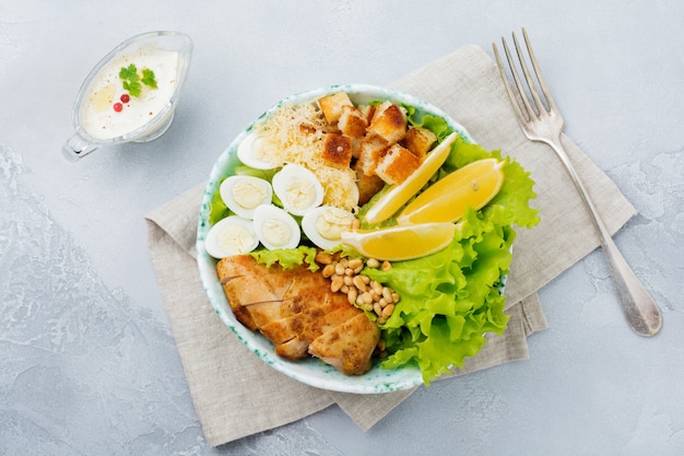 Traditional Caesar Salad with quail eggs and pine nuts in a light ceramic bowl On a gray stone or concrete surface