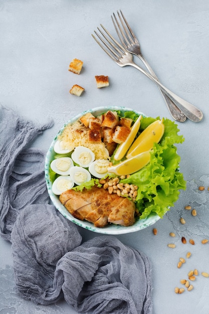 traditional caesar salad with quail eggs and pine nuts in a light ceramic bowl on a gray stone