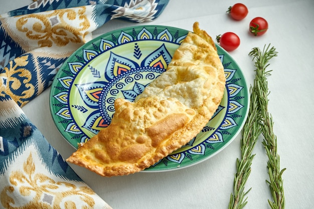 The traditional Caucasian dish is Cheburek, a fried pie in oil with different fillings, mainly meat or cheese on a blue plate.