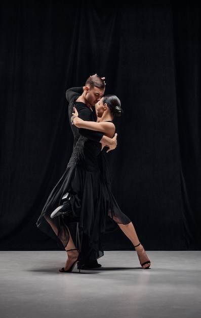 Foto coreografia tradizionale ballerini professionisti di tango uomo e donna che si esibiscono in costumi di scena neri su sfondo nero