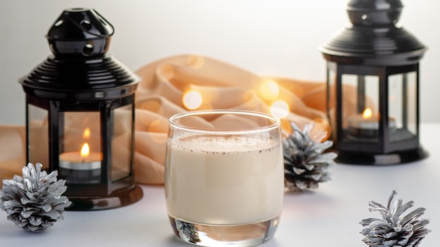 Traditional Christmas cocktail Eggnog with eggs, alcohol, grated nutmeg and cinnamon closeup. Sweet traditional drink for Christmas and winter on table with red decorations and golden pine cones