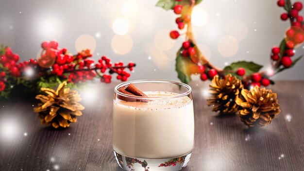 Traditional Christmas cocktail Eggnog with eggs, alcohol, grated nutmeg and cinnamon closeup. Sweet traditional drink for Christmas and winter on table with red decorations and golden pine cones