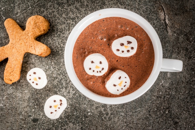 Traditional Christmas drink idea. Hot chocolate mug with marshmallow, decorated in the form of snowmen, On black stone table top view 