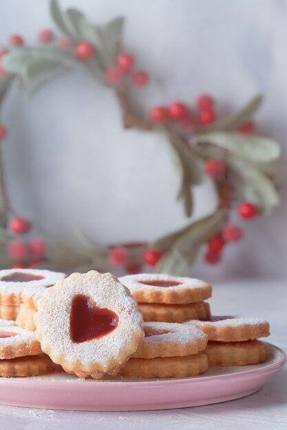 Traditional Christmas Linzer cookies filled with red jam on light table with Xmas decorations